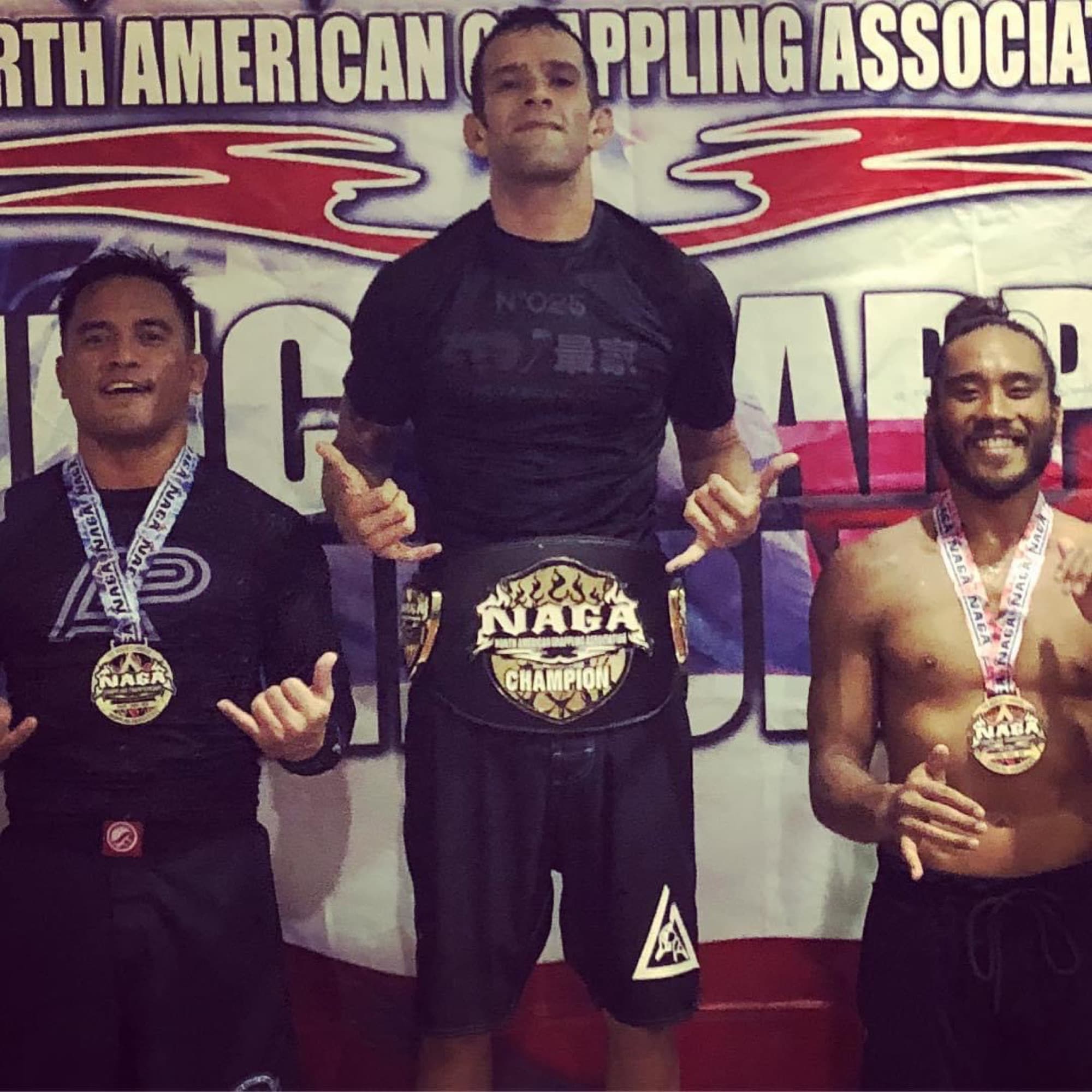 Joel Bouhey at the center of a podium holding a champion belt.