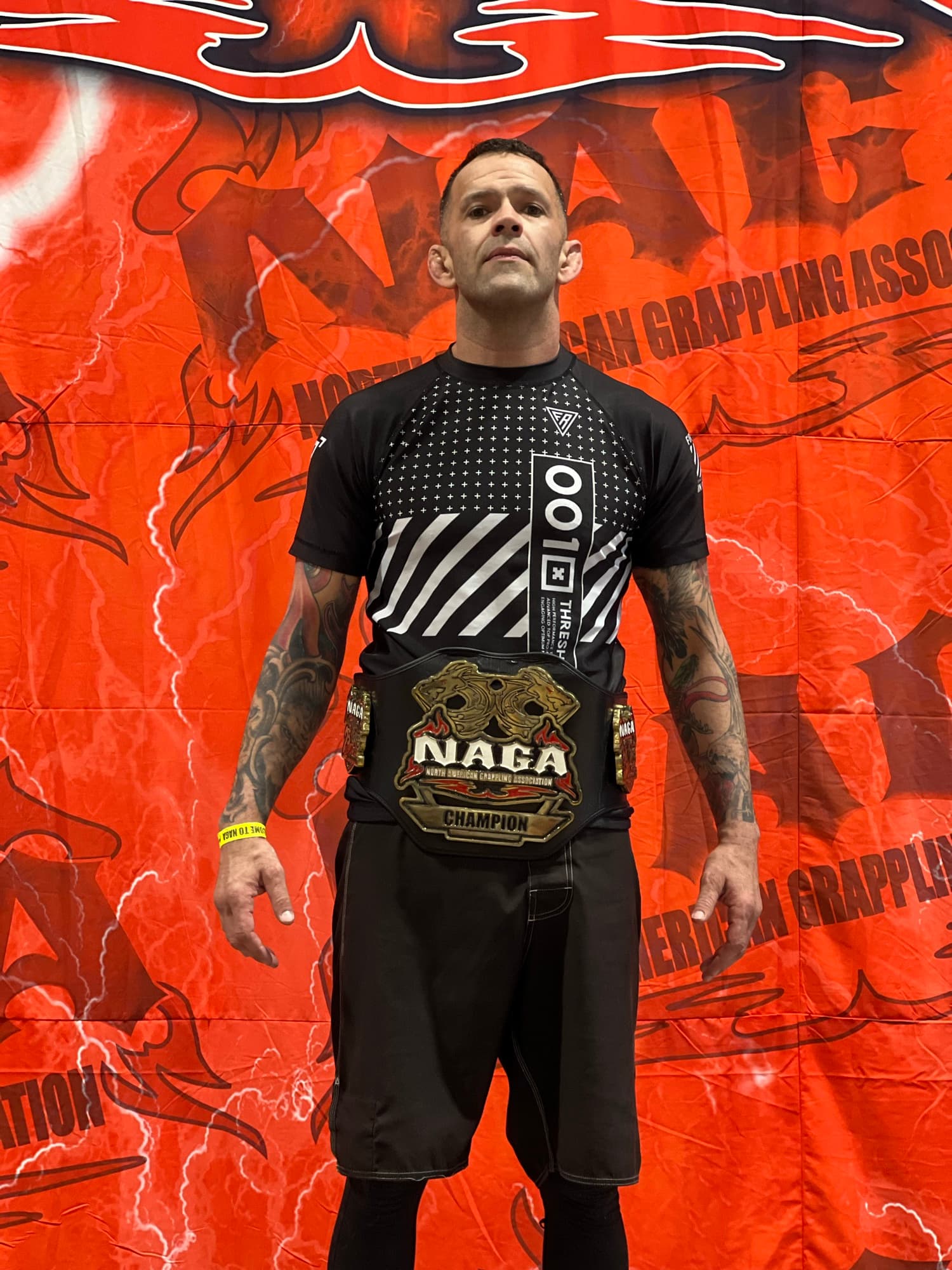 Joel Bouhey with a NAGA champion belt in front of an orange NAGA backdrop.