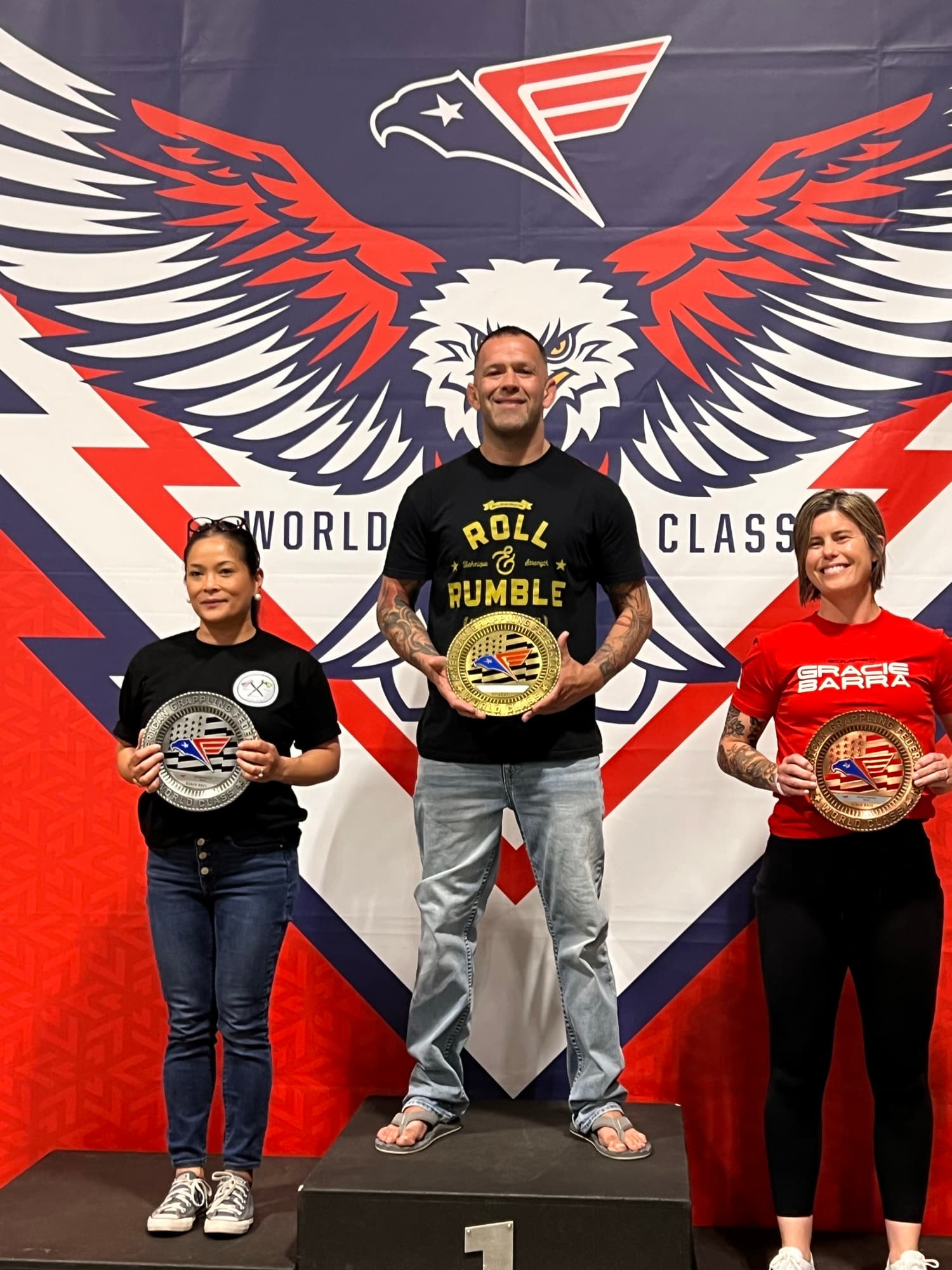 Joel Bouhey at the top of a podium holding a plaque.
