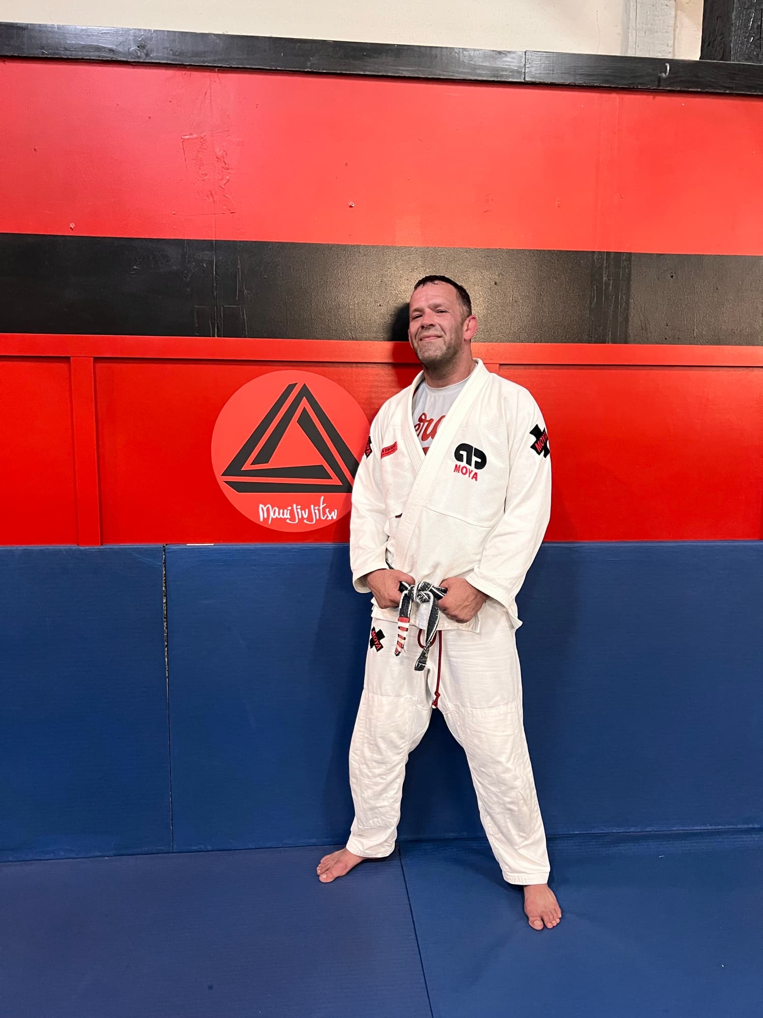 Joel Bouhey standing in a white gi on red and blue mats.